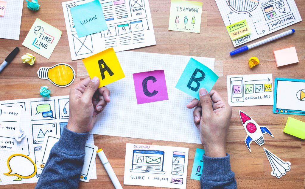 An aerial view of a desk strewn with sticky notes and sketches, with a man holding a sticky note labelled A and B in each hand