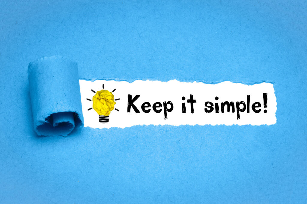 The phrase Keep it simple! next to a lightbulb icon on a white background that looks like it is being revealed by tearing off a layer of blue paper above it