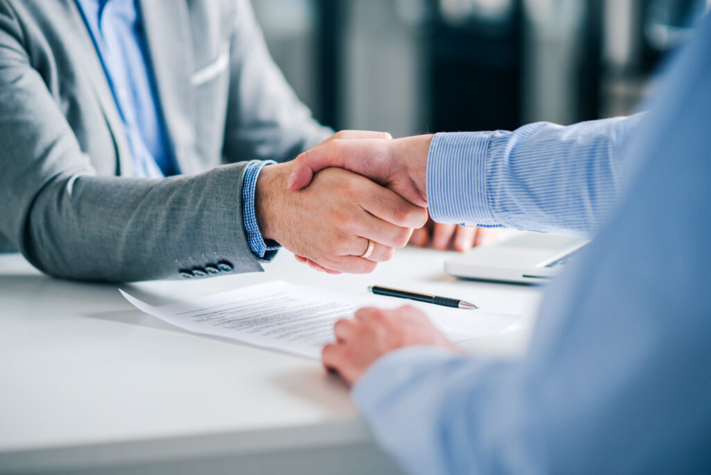 A close up of two people wearing business attire, shaking hands over a desk