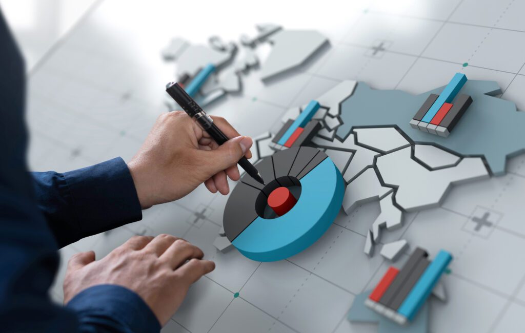 A hand hovers a pen over a range of charts on a world map