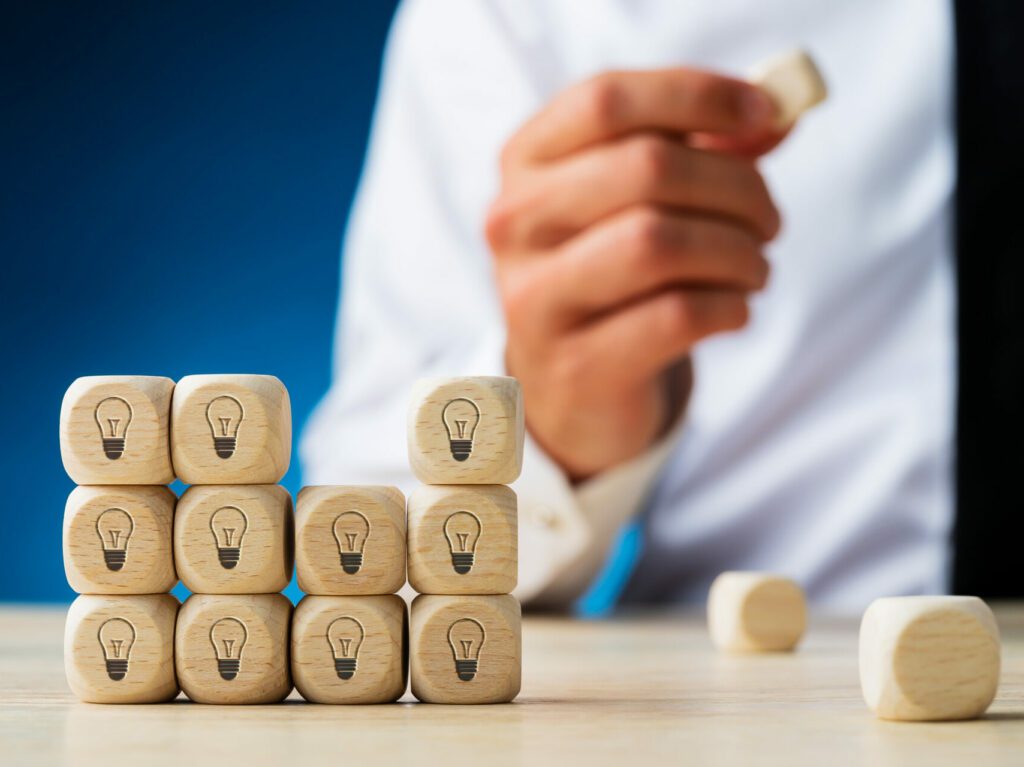 A hand holds a wooden block taken from a stack of wooden blocks, each with a light bulb icon printed on