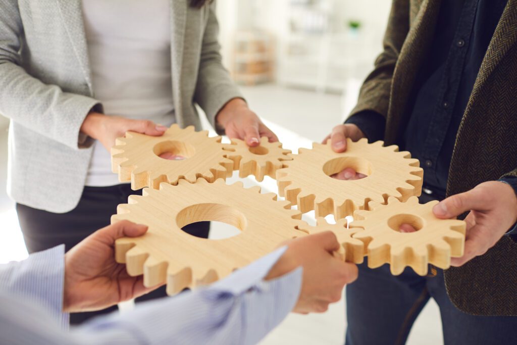 Three people hold together large wooden cogs