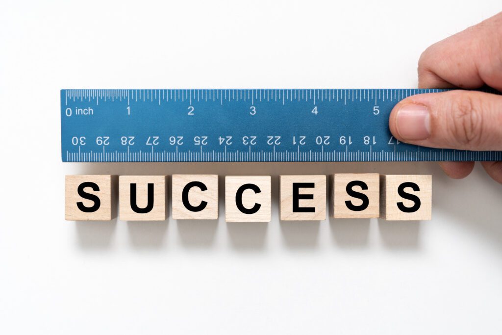 A hand holds a ruler beside a row of wooden blocks that spell SUCCESS