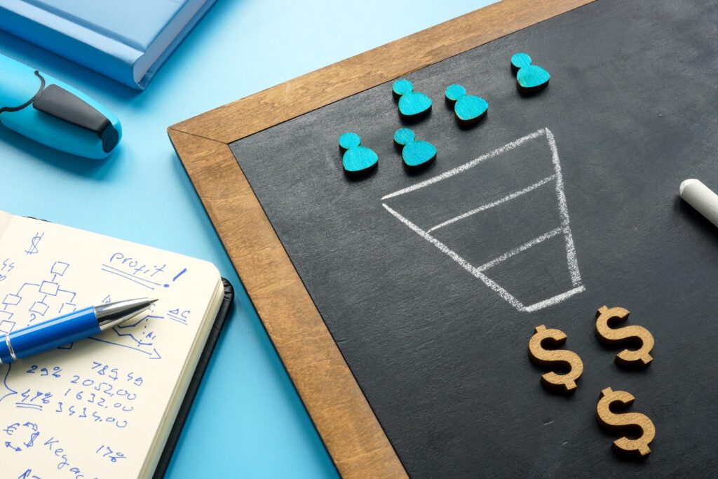 A funnel drawn on a chalkboard with a group of people icons at the top and dollar signs at the base