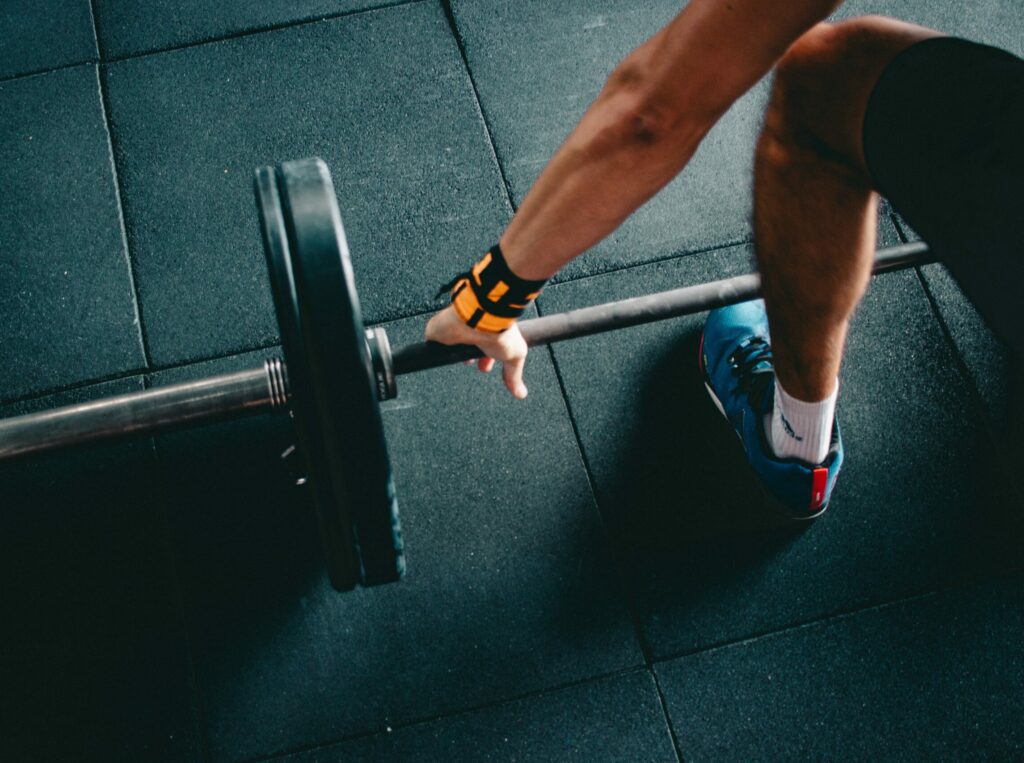 A close-up of a person squatting to lift a barbell, with only an arm and leg in the frame